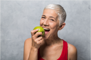 Older woman taking bite out of an apple Family Dentist Huntsville